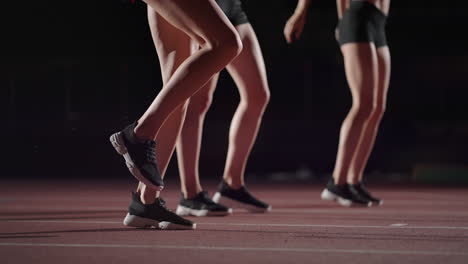 Three-women-athletes-prepare-for-a-track-race-in-a-dark-stadium-with-streetlights-on.-Time-lapse-footage-of-warm-up-and-concentration-of-a-group-of-women-before-the-race-on-the-track